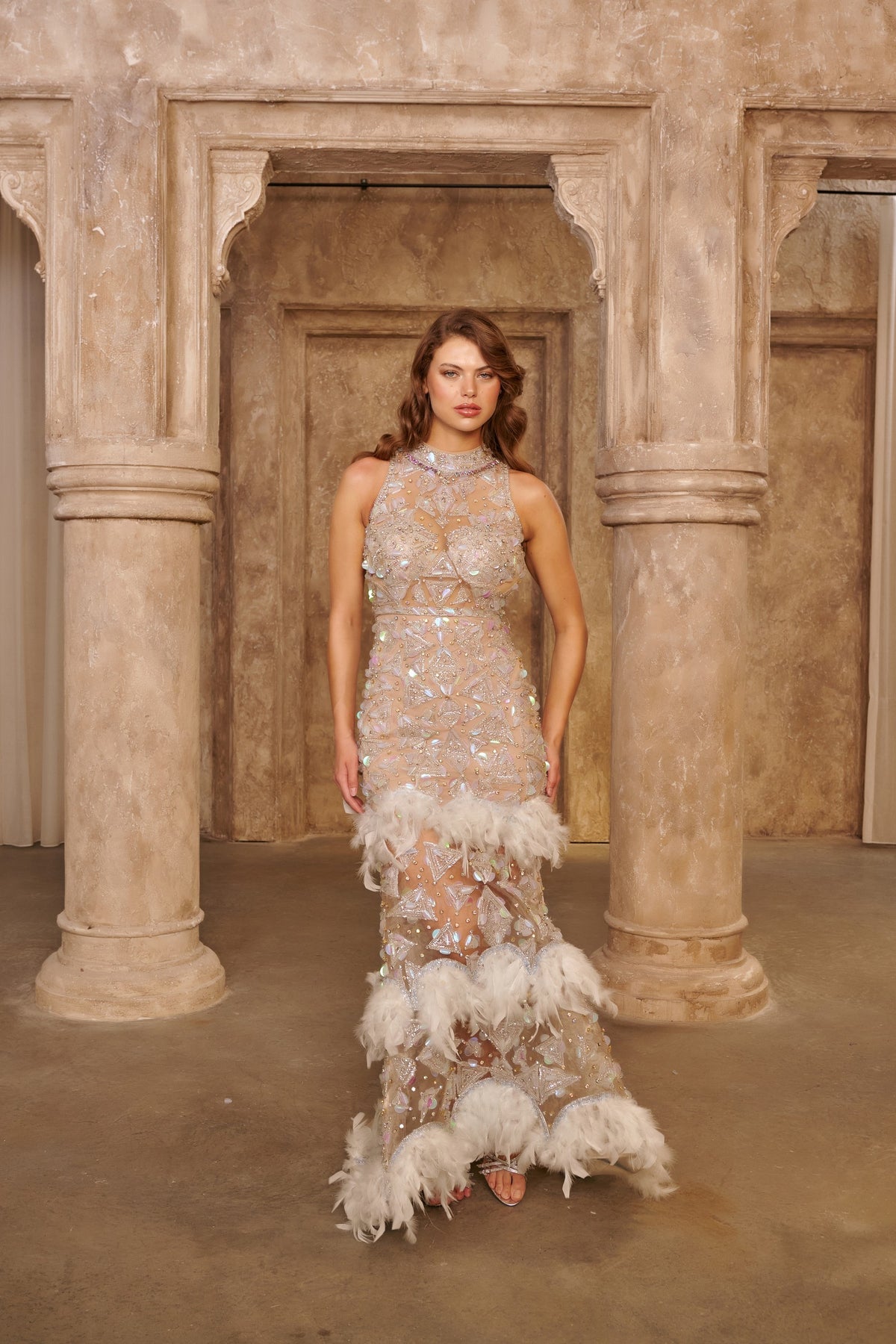 Crystal Feather ivory evening gown with a sheer fitted silhouette, silver crystal embellishments and layered feather trim.