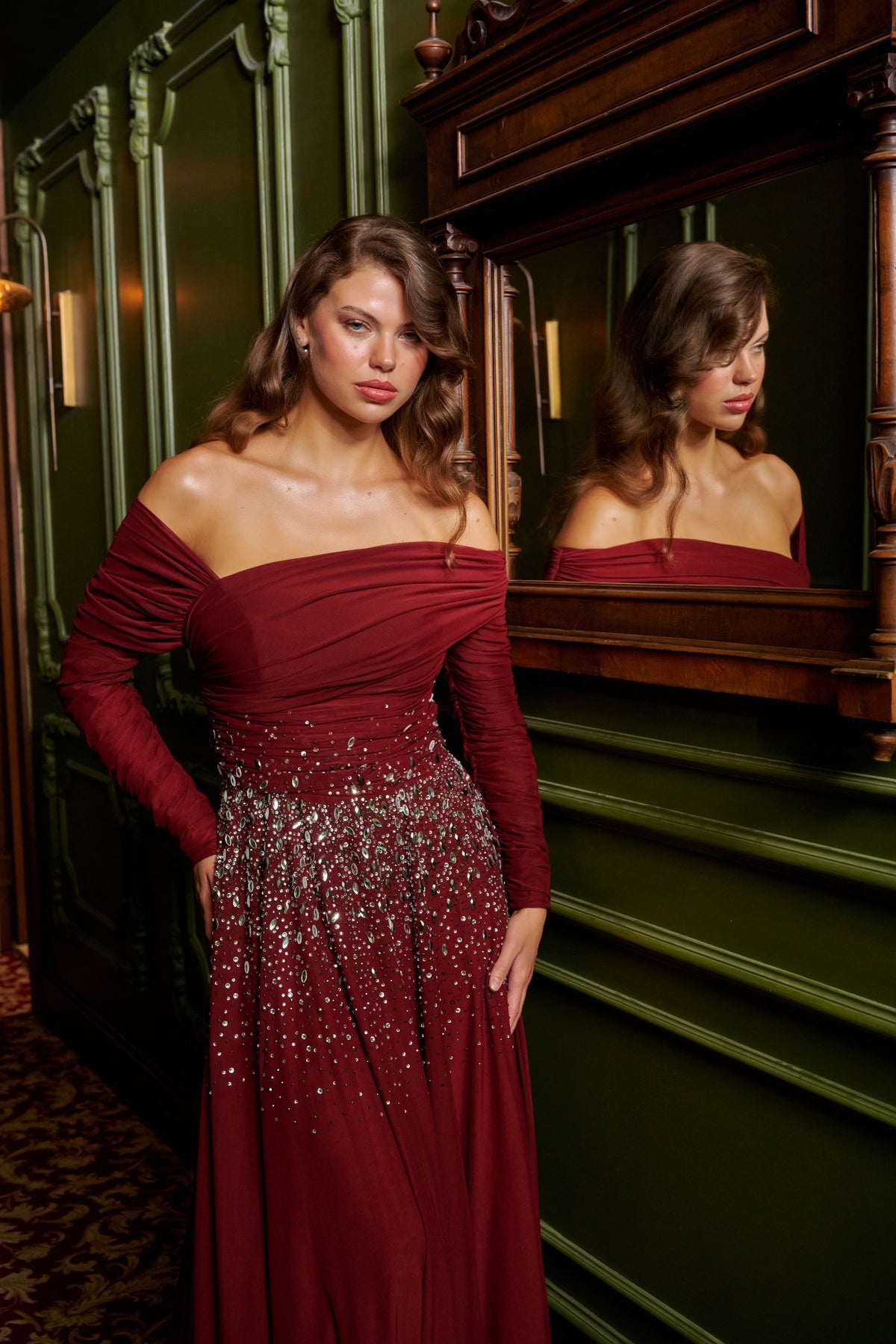 Ruby Drape burgundy off-the-shoulder evening dress with long sleeves, crystal waist embellishments and a flowing floor-length skirt.