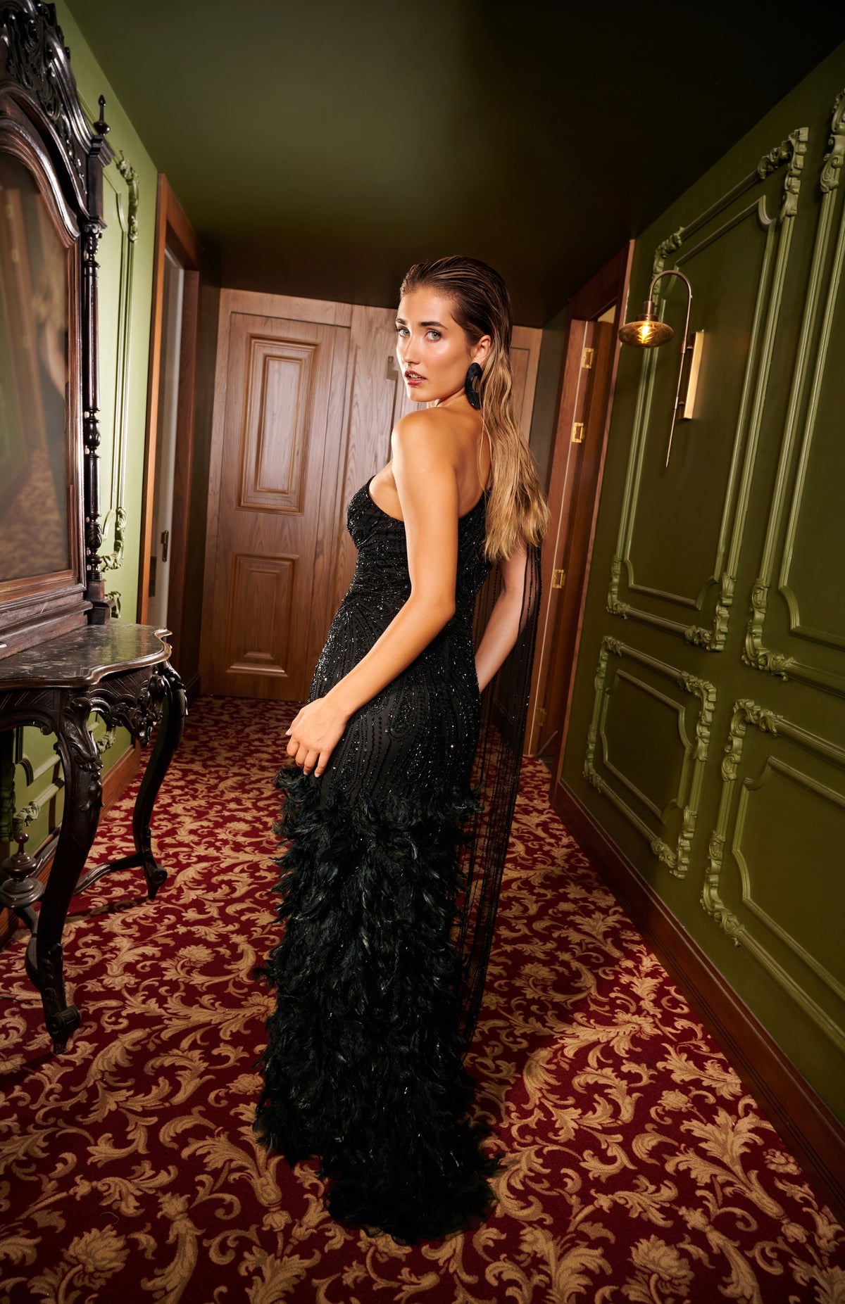Black Swan one-shoulder black embellished evening gown with a sheer cape sleeve, feather trim and thigh-high slit.