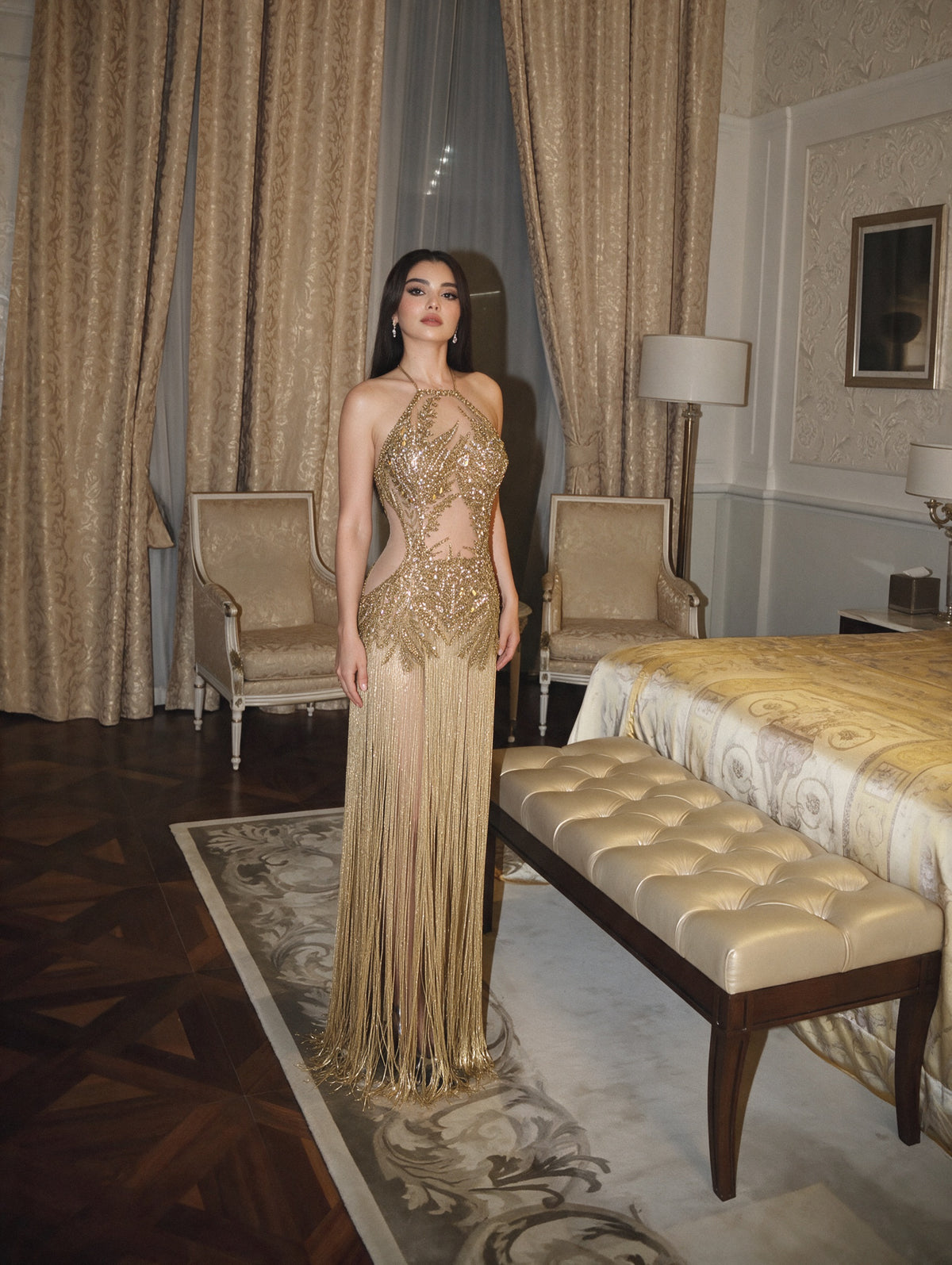 A gold fringe gown standing in a panelled suite with silk curtains.