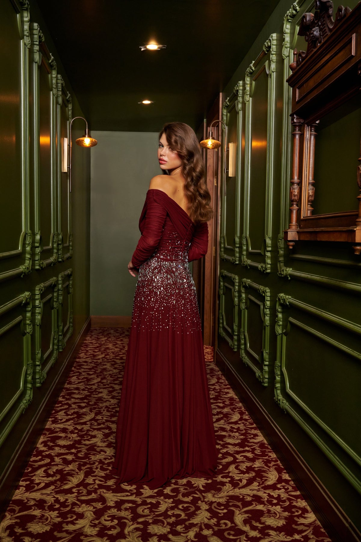 Ruby Drape burgundy off-the-shoulder evening dress with long sleeves, crystal waist embellishments and a flowing floor-length skirt.