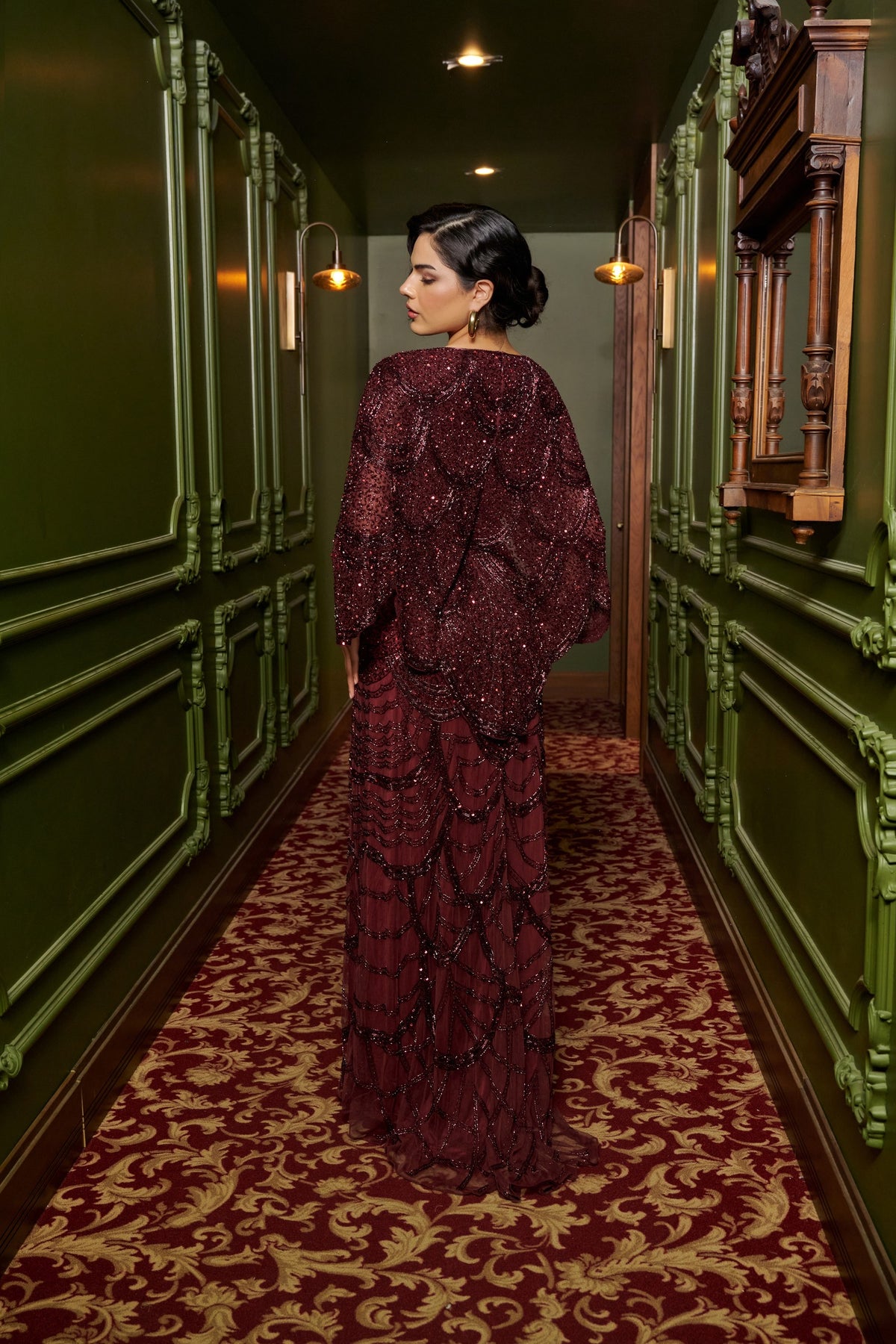 Ruby Grace burgundy embellished evening gown with a sheer cape overlay, flowing sleeves and a floor-length fitted silhouette.