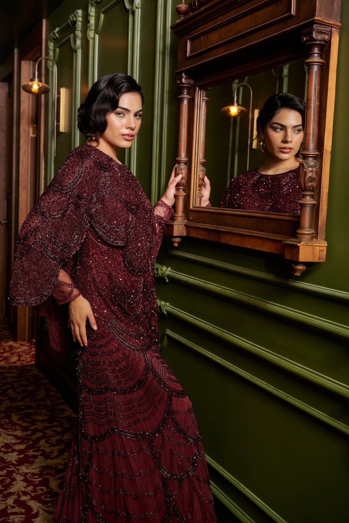 Ruby Grace burgundy embellished evening gown with a sheer cape overlay, flowing sleeves and a floor-length fitted silhouette.