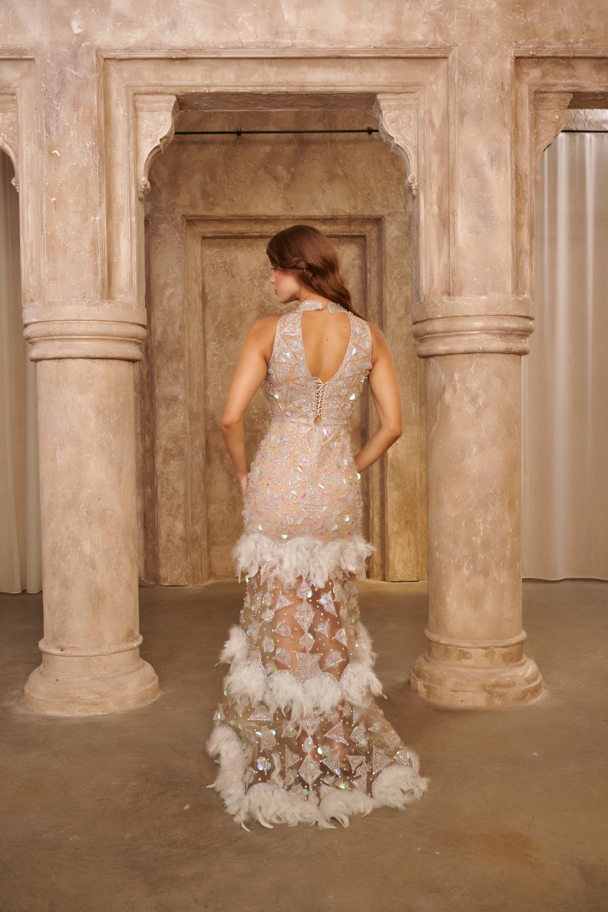 Crystal Feather ivory evening gown with a sheer fitted silhouette, silver crystal embellishments and layered feather trim.