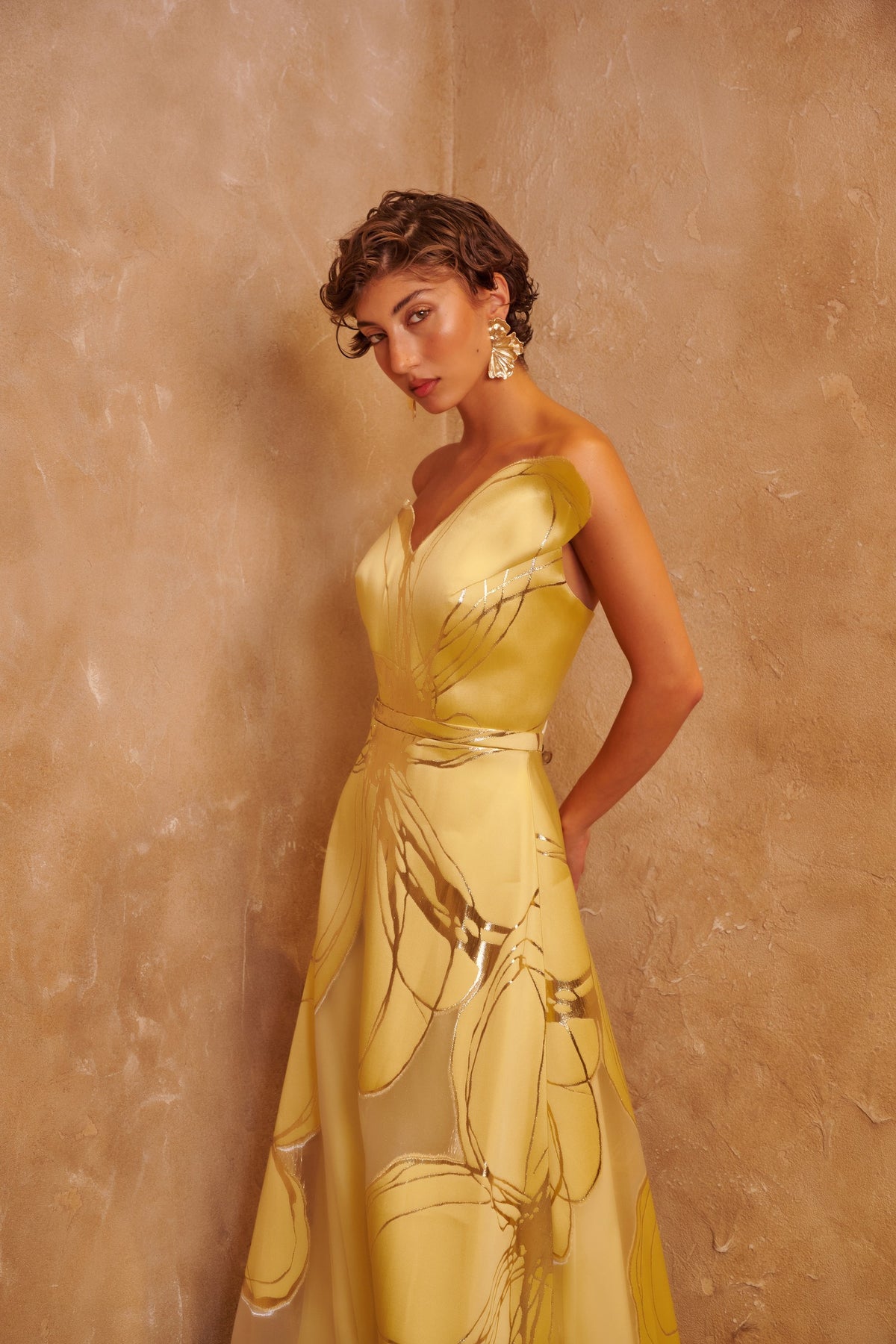 Golden Orbit yellow gown with a sculpted one-shoulder neckline, metallic swirl details and a defined waist.